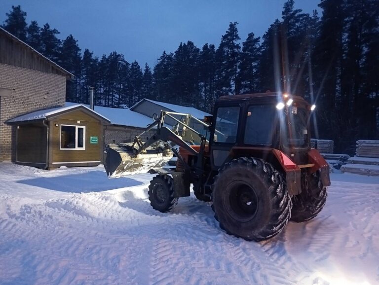 Traktor lükkab lund hoovis kontorihoone kõrval