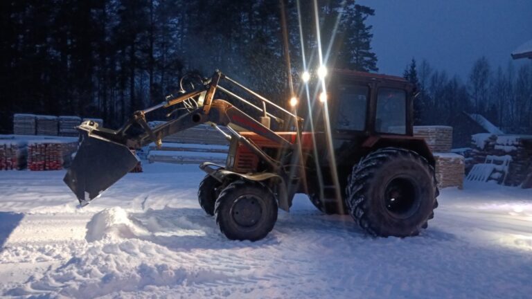 Traktor kopaga lund lükkamas saematerjali virnade kõrval
